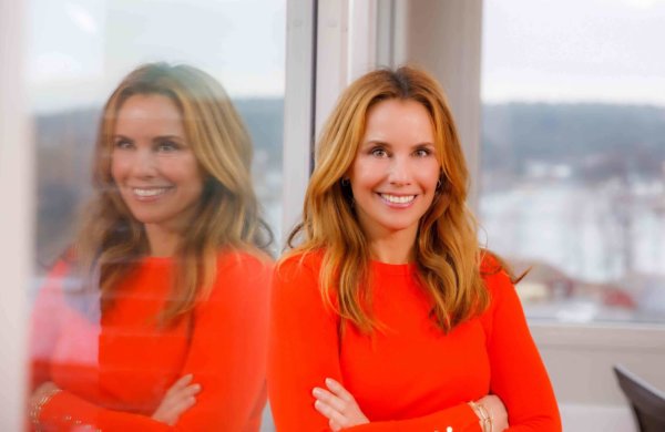 Kvinne med knall oransje genser lener seg mot vindu og smiler