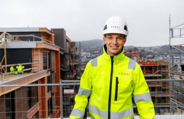 Blid mann med gul refleksjakke og hvit hjelm på en byggeplass