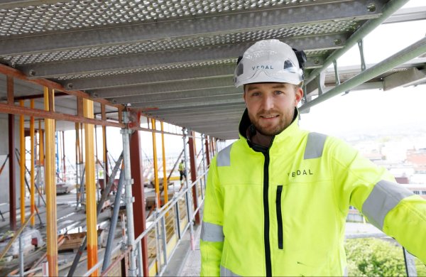 Mann i gul vernejakke og hvit hjelm på byggeplass